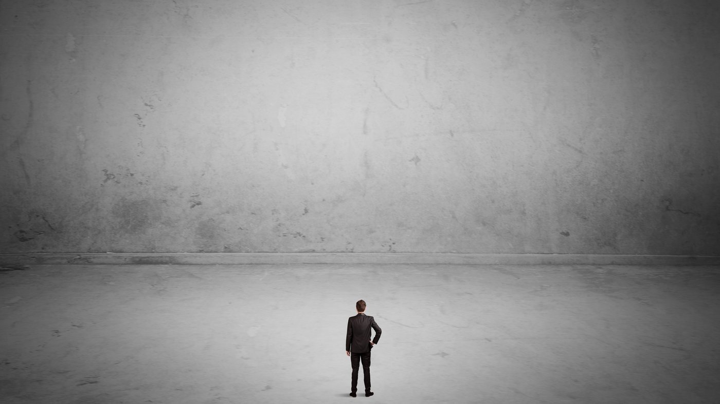 A small lone figure standing before a vast bare wall