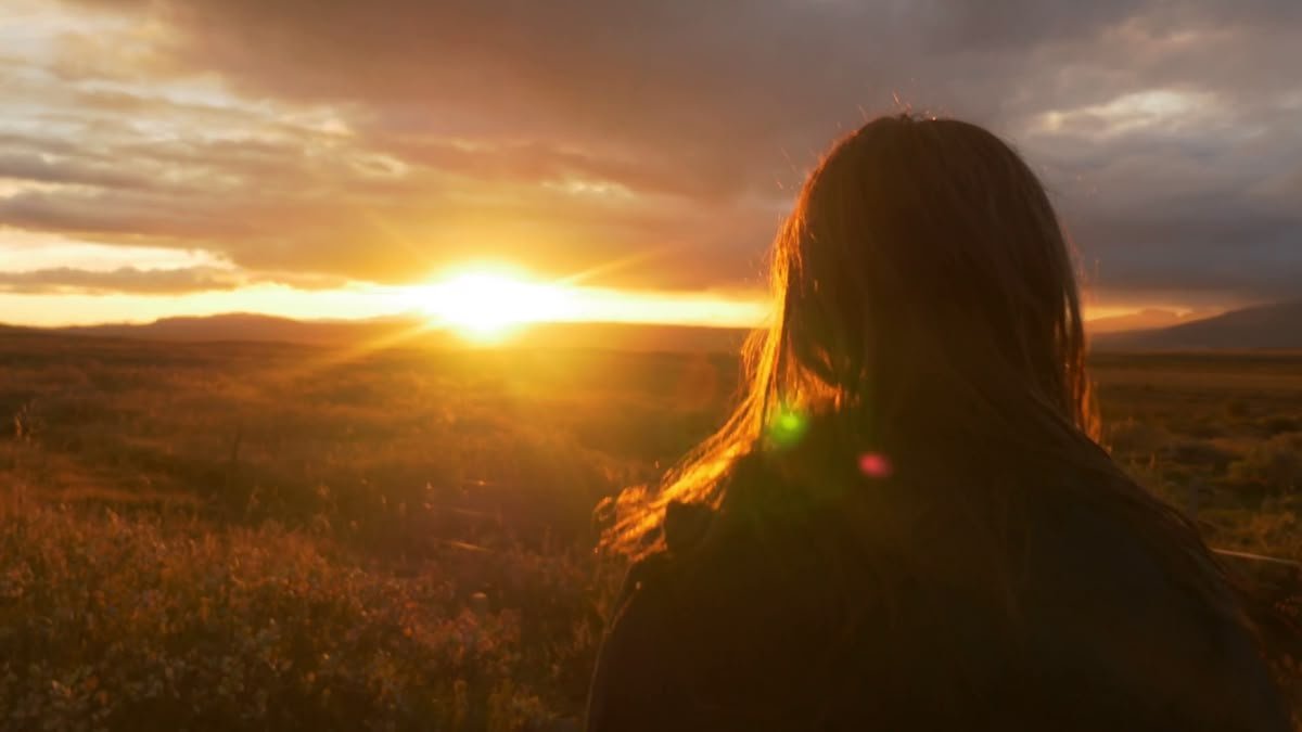 A woman seen from behind watching the sun set over open moorland