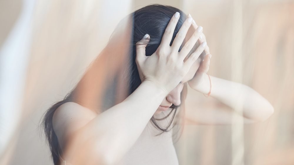 A woman holding her head in both hands, the image softly blurred as if dizzy