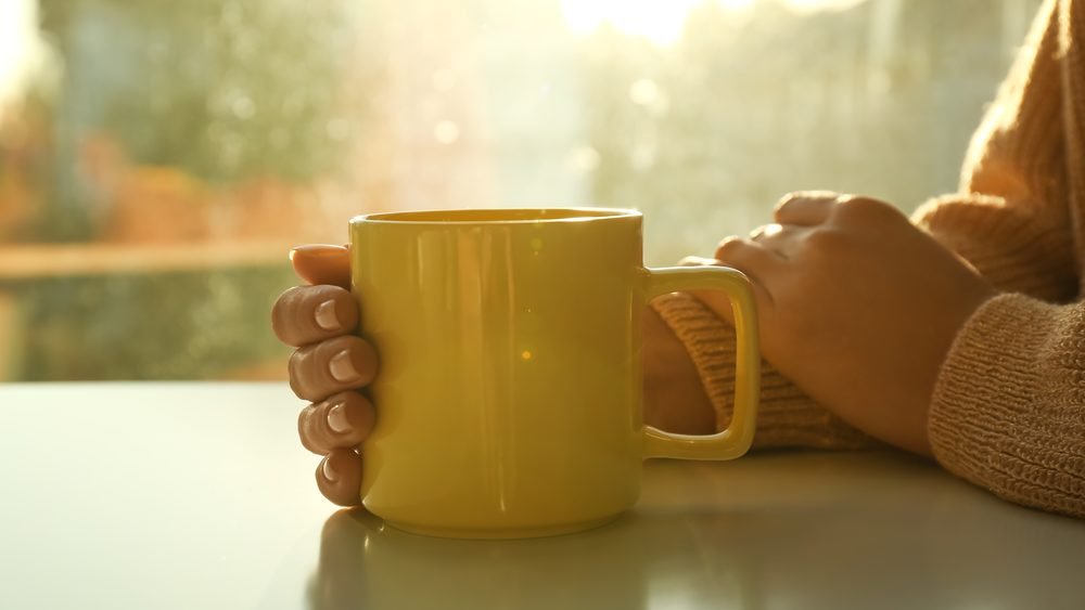 Hands wrapped around a warm mug of tea on a table in soft morning light