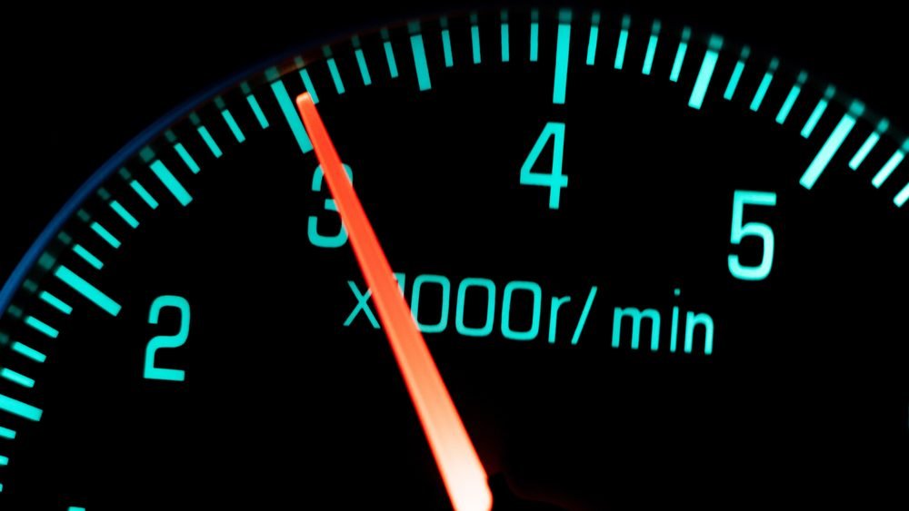 A glowing car rev counter with the needle climbing, an engine working hard