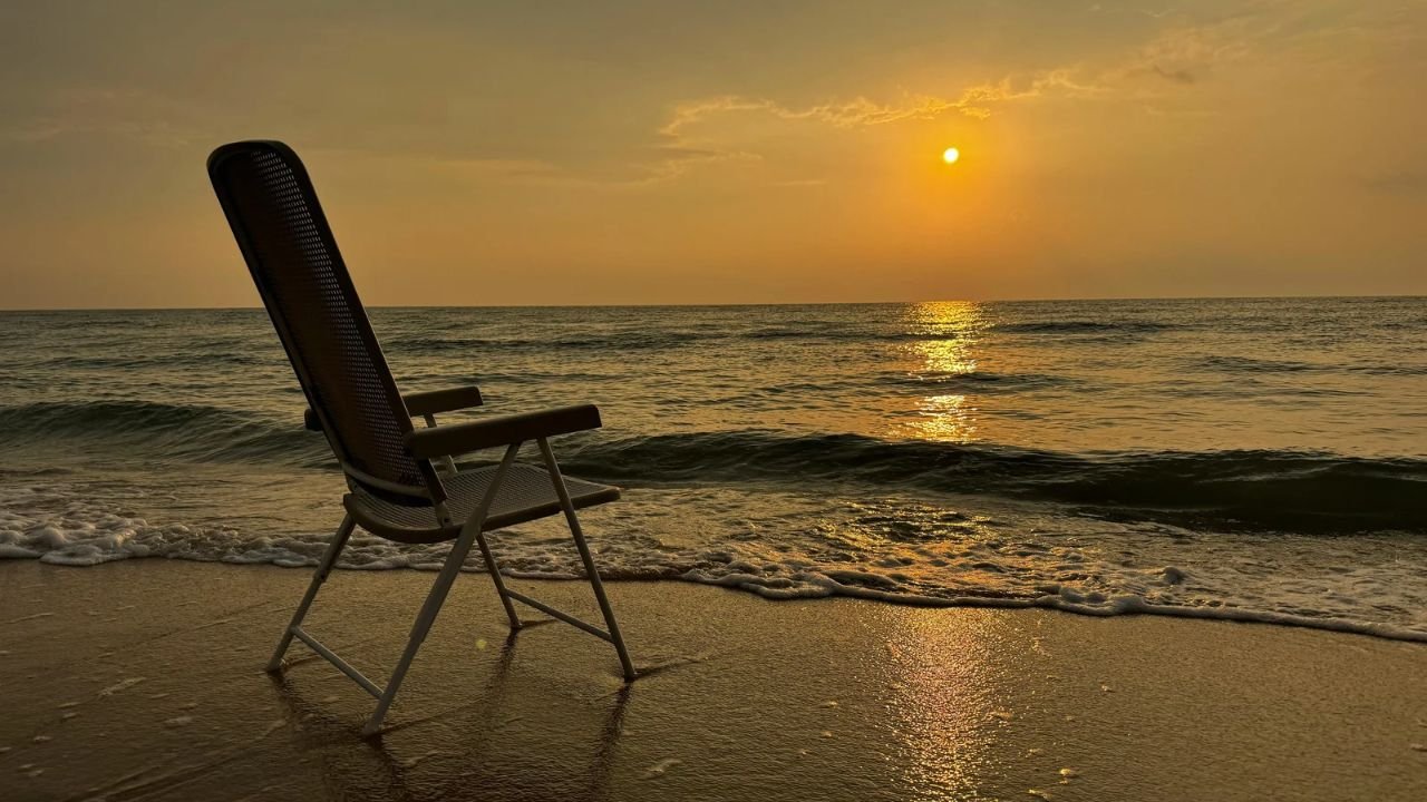 An empty folding chair at the water’s edge on a beach at sunset
