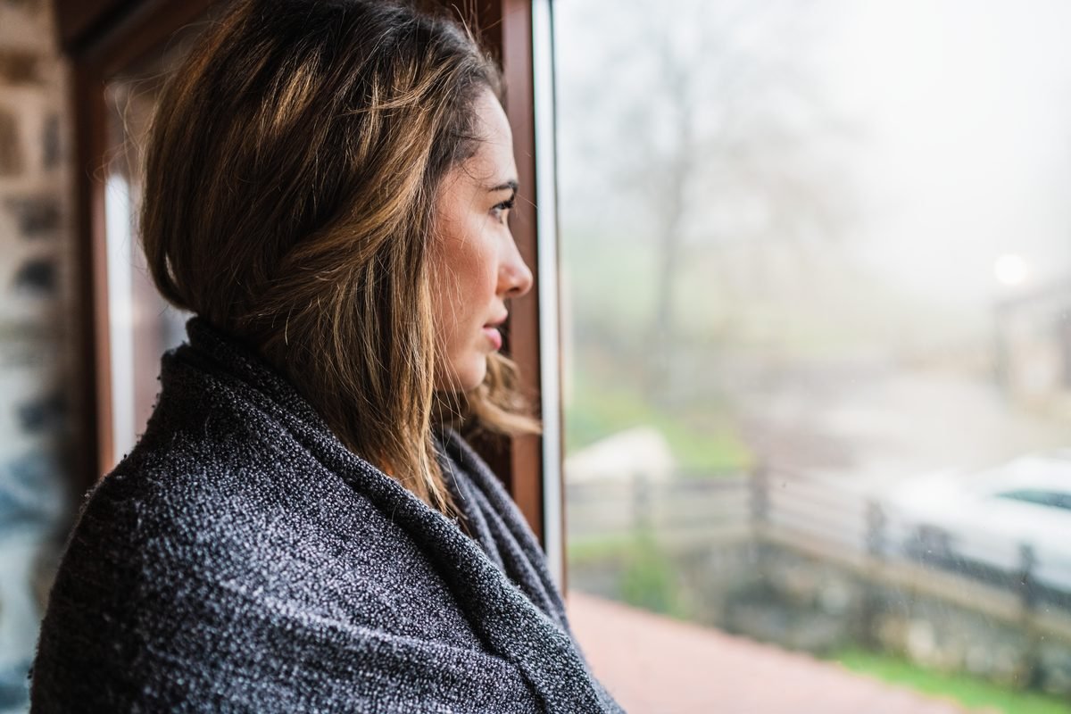A person wrapped in a shawl gazing thoughtfully out of a window